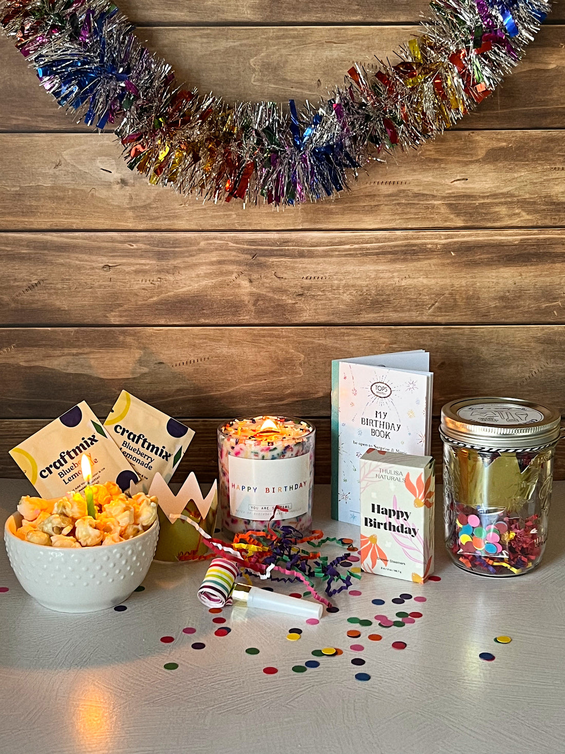 Birthday Crate featuring festive popcorn, a birthday candle, celebration book, shower steamers, and a confetti-filled jar with colorful decorations.